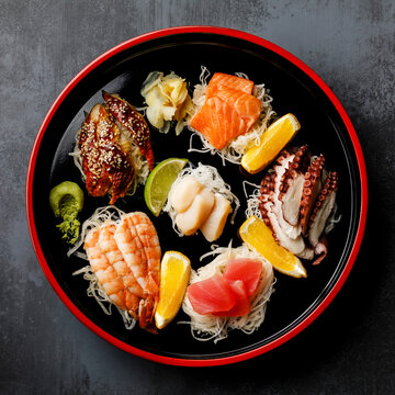 Sashimi sushi set with daikon and lemon on traditional Japan black Sushioke round plate on dark background