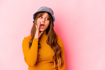 Young caucasian woman wearing fishermans hat isolated is saying a secret hot braking news and looking aside