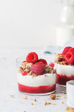3 layered yogurt parfaits on a white background with home-made granola, raspberry purre and fresh raspberries and cranberries.