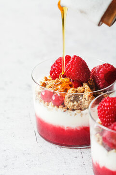 Honey pour on a yogurt parfait with home made granola, raspberry puree and fresh raspberries and cranberries.