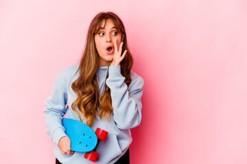 Young skater woman isolated on pink background is saying a secret hot braking news and looking aside