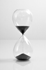 Hourglass transparent crystal black sand falling down vertical old vintage clock isolated on white background 