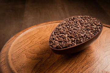 Stuffed chocolate easter egg with grated chocolate on the top on a wooden stand on a wooden table.
