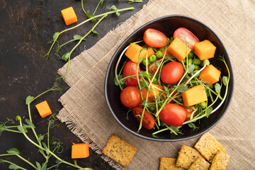 Vegetarian vegetable salad of tomatoes, pumpkin, microgreen pea sprouts on black concrete background. Top view.