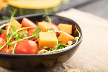 Vegetarian vegetable salad of tomatoes, pumpkin, microgreen pea sprouts on black concrete background. Side view, selective focus.