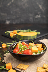 Vegetarian vegetable salad of tomatoes, pumpkin, microgreen pea sprouts on black concrete background. Side view, copy space.