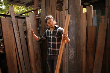 Young Caucasian carpenter man is choosing plank of wood in his own garage style workshop for hobby with copy space