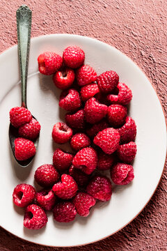 Fresh raspberries on a plate with a spoon sitting on a terra cotta colored background.