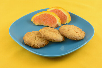 Orange zest butter cookies with orange slices on blue snack plate on yellow tablecloth