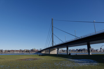 Outdoor sunny view of natural riverside of Rhine River covered with slush snow and ice pond with people do winter recreation and background cityscape of Düsseldorf, Germany in winter season.