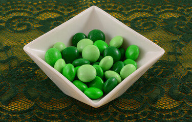 Green candy coated dark chocolate mint candy for Saint Patrick Day in white candy dish on green lace table runner on yellow tablecloth