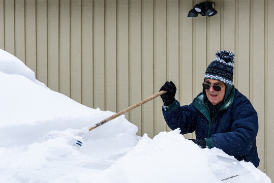 Senior Man Cleaning Snow Off The Hood Of A Truck After A Fresh Snowfall
