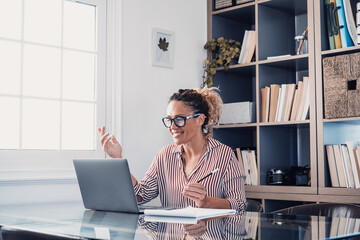 One young woman working at home in the office with laptop and notebook taking notes talking in a video conference. One businesswoman calling communicating