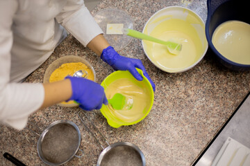 Woman confectioner in uniform pouring liquid matcha tea chocolate on table from bowl at cuisine