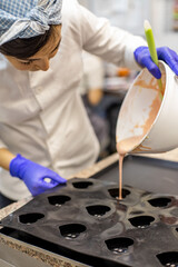 Woman confectioner pouring liquid chocolate into rubber mold tray for cooking pastry candy
