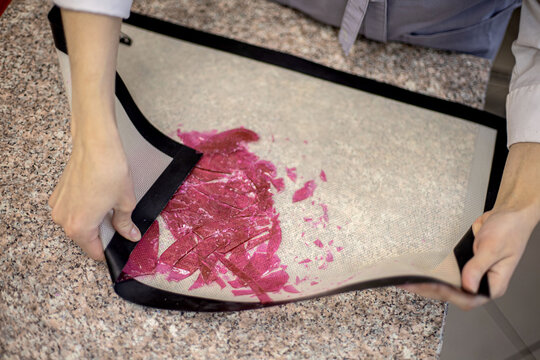 Closeup female hands crushing dyed pink isomalt caramel for cake decor on confectionery mat