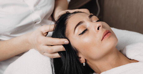 Obraz na płótnie Canvas close up photo of a head massage session done at the spa center to a brunette woman lying with closed eyes