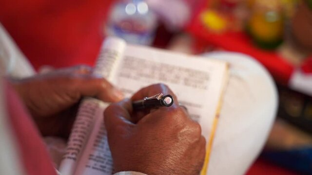 closeup hands of an asian Indian male writing with pen on a book printed in foreign language