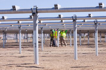 workers on construction site standing under metal tubing grid at solar farm installing solar panels