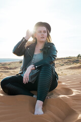 woman sitting in the desert sand dunes in black leather in black hat