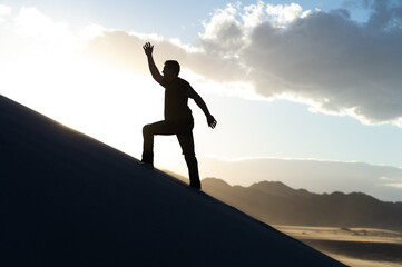 silhouette man running up a sand dune in the desert at sunset