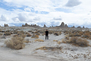 Man in black alone in the desert with rock formations in the background