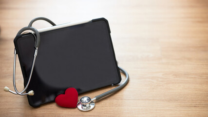 A digital tablet, stethoscope, and a red heart are placed on a wooden floor.