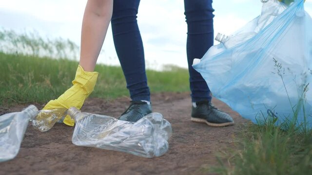 volunteer collects plastic trash in the park. recycle plastic clean bottle cleanup ecology concept blurred background. girl volunteer gloves collects plastic bottles and glasses in a trash bag