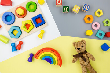 Wooden toys, blocks, a bear on yellow gray background. Trendy cute baby first toys. Eco-friendly, plastic-free set of accessories for kids. Toys for kindergarten, preschool or daycare. Close up	