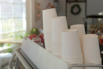 A lot of white disposable paper cups on coffee machine with cofe shop background. The stack of paper cup in the cafe. close up recycle white paper cups on coffee machine