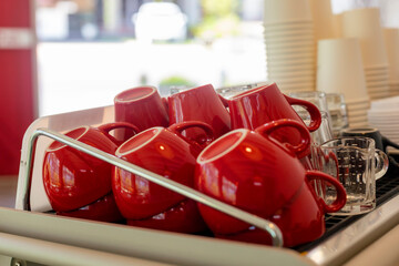 Obraz na płótnie Canvas Lots of ceramic red coffee cups on espresso machine shelf in coffee shop. Selective focus. Red coffee cups on coffee machine in cafe soft focus selective red cup row two.