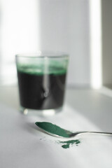 metal spoon with spirulina powder and drink with spirulina in a glass beaker on a white background. Selective focus on the main object - the spoon.