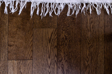 Edge of blanket against a wooden surface; tassels of mat on wooden floor
