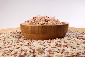 Fototapeta na wymiar Cooked and raw mixed low glycaemic index healthy rice grain basmati millet buckwheat red rice in wooden bowl over wooden plate on white background