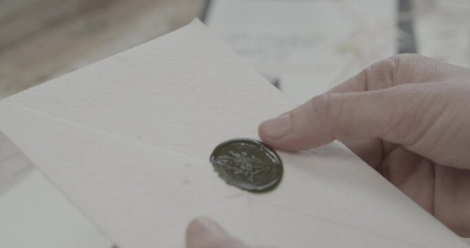 A person checking the hardened sealing wax on an envelope. Handheld shot.
