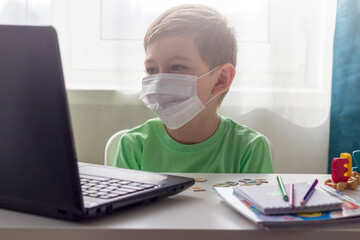 Distance learning, online education. Social distance, self-isolation during quarantine. Preschooler or schoolboy in medical mask studying at home with laptop, doing homework for development school