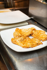A view of a plate of seasoned chicken breast on the counter of a restaurant kitchen.