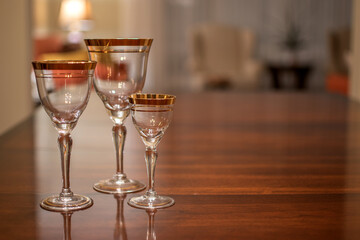 Three empty vintage, gold rimmed wine glasses of various sizes on a table.