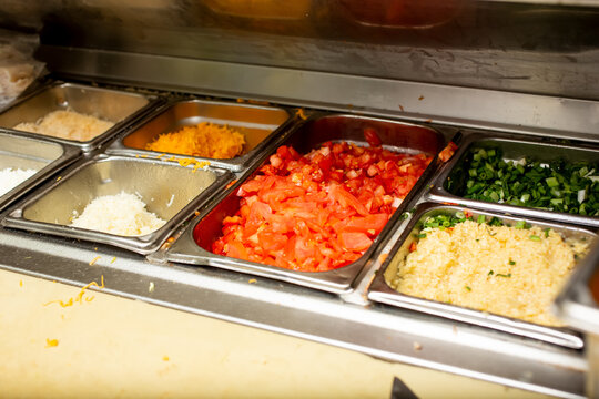 A View Of Food Organized In Steam Containers In A Food Preparation Station, In Side A Restaurant Kitchen Setting.