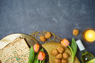 Jewish holiday Passover background with matzah, seder plate, wine and tulip flowers on dark table