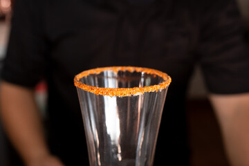 A closeup view of a glass rim garnished with chili lime salt, sitting in front of a bartender, in a...