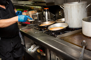 A view of a line cook preparing several meals on the stove in a restaurant kitchen setting.