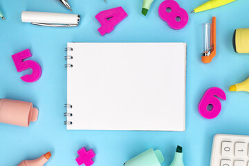 A notebook with a white blank sheet lies on a blue background among the school supplies. Pink...