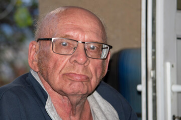 Old grandfather with glasses is bald. Looks into the camera on a sunny autumn day.