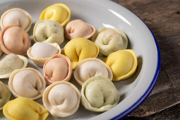 Traditional Russian dumplings made from multi-colored dough. Dumplings on a wooden board in an enamel plate. Cooking concept.