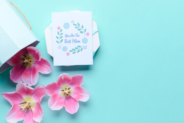 Box with beautiful flowers and greeting card for Mother's Day on color background