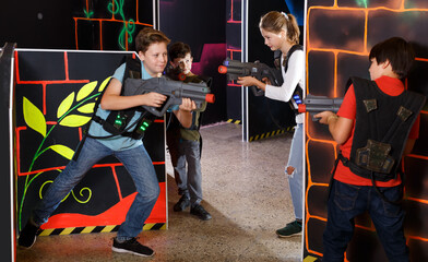 Laughing teen kids aiming laser guns at other players during lasertag game in dark room