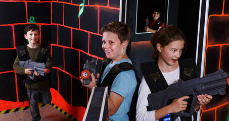 Fototapeta na wymiar Portrait of excited active teen boy and girl aiming laser gun at other players during lasertag game in dark room