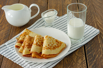 Stack of pancakes or crepes on a plate served with sour cream. Traditional food for the Russian pancake week. Wooden background