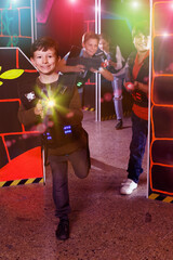 sportive young boy aiming laser gun at other players during lasertag game in dark room